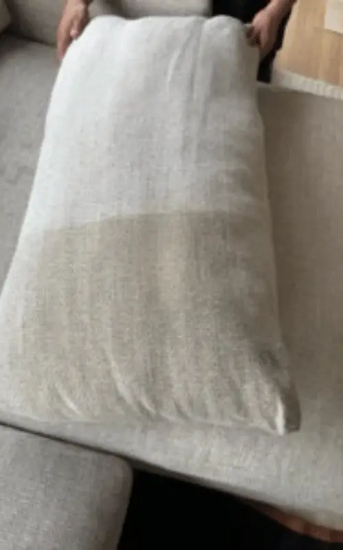 Hands carefully placing a freshly cleaned, light grey cushion back onto a sectional sofa, showcasing the pristine results of professional upholstery cleaning and the care taken with customer furniture.