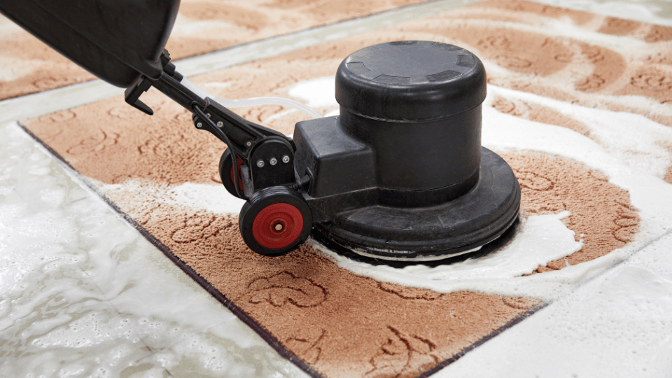 Close-up of a heavy-duty rotary floor machine applying eco-friendly cleaning foam to deep clean a textured area rug. The image highlights the mechanical agitation process used to effectively lift deep-set dirt and allergens for thorough rug cleaning.